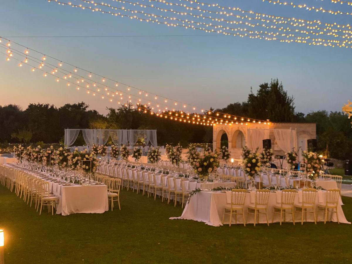 Tavoli lunghi sotto fili di luci in una masseria al tramonto